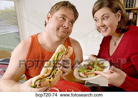 Woman offering her husband a salad instead of sandwich View Large Photo Image Picture - Woman offering her husband a salad instead of sandwich. Fotosearch