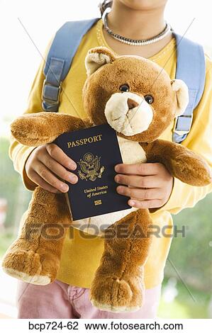 Stock Image - Young girl holding teddy bear and passport. Fotosearch