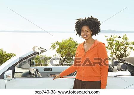 Stock Image - African woman next to convertible car. Fotosearch