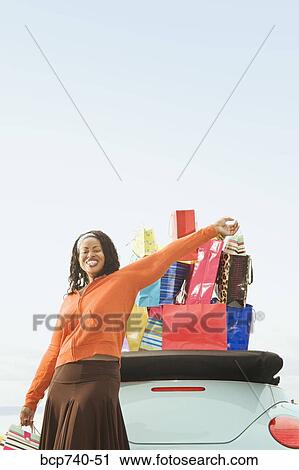 Stock Image - African woman next to convertible with shopping bags. Fotosearch
