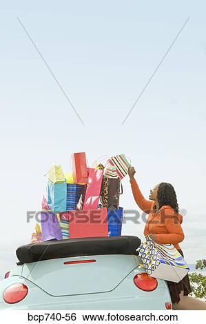 Stock Photograph - African woman next to convertible with shopping bags. Fotosearch