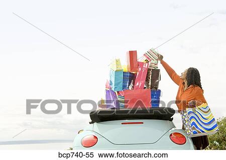 Stock Photography - African woman next to convertible with shopping bags. Fotosearch