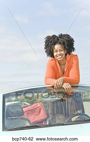 Stock Image - African woman standing in convertible car. Fotosearch