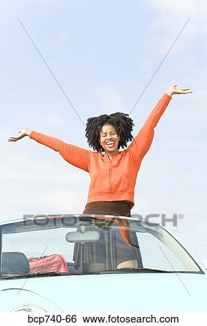 Stock Photograph - African woman with arms raised in convertible car. Fotosearch