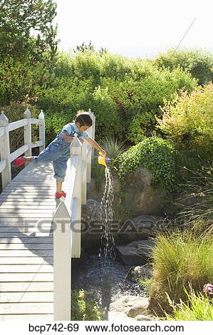 Asian boy pouring water over bridge railing View Large Photo Image Stock Photo - Asian boy pouring water over bridge railing. Fotosearch
