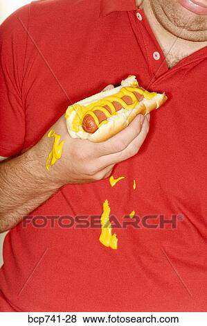 Stock Photo - Man holding hotdog and spilling mustard on shirt. Fotosearch