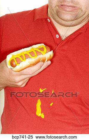 Stock Photography - Man holding hotdog and spilling mustard on shirt. Fotosearch