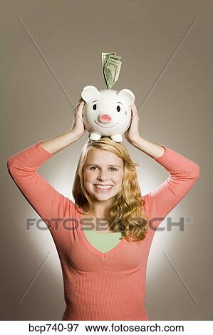Teenage girl holding piggy bank on head View Large Photo Image Stock Photo - Teenage girl holding piggy bank on head. Fotosearch