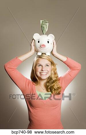 Teenage girl holding piggy bank on head View Large Photo Image Stock Photo - Teenage girl holding piggy bank on head. Fotosearch