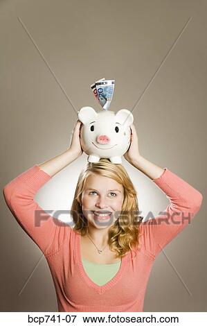 Teenage girl holding piggy bank on head View Large Photo Image Stock Photo - Teenage girl holding piggy bank on head. Fotosearch