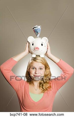 Teenage girl holding piggy bank on head View Large Photo Image Stock Photo - Teenage girl holding piggy bank on head. Fotosearch