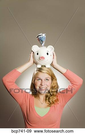 Teenage girl holding piggy bank on head View Large Photo Image Stock Photo - Teenage girl holding piggy bank on head. Fotosearch