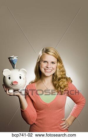 Stock Image - Teenage girl holding piggy bank with money. Fotosearch
