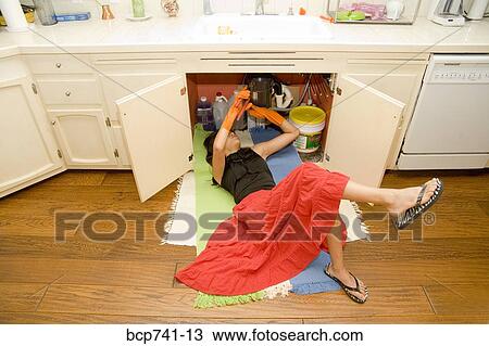 Stock Image - Woman fixing plumbing under sink. Fotosearch