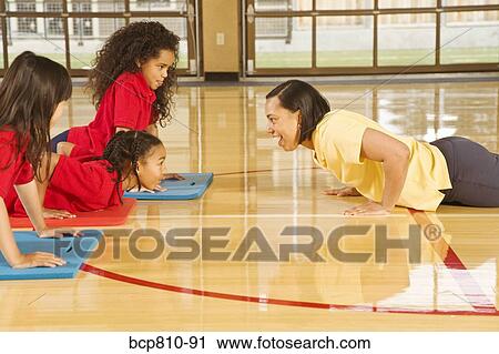Stock Image - African female gym teacher teaching yoga to multi-ethnic students. Fotosearch