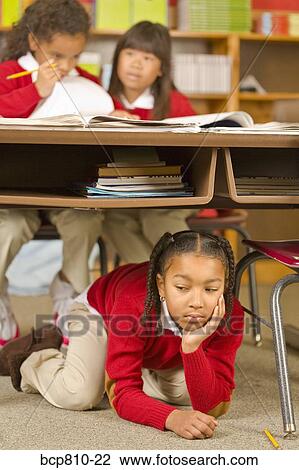 Stock Image - African girl sitting under school desk. Fotosearch