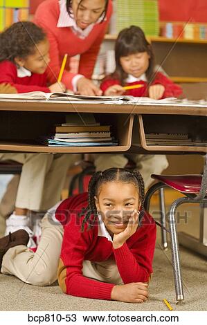 Stock Image - African girl sitting under school desk. Fotosearch