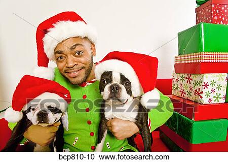 Stock Image - African man an dogs wearing Santa Claus hats. Fotosearch