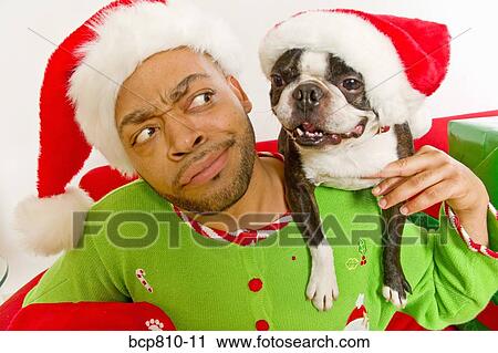 Stock Image - African man and dog wearing Santa Claus hats. Fotosearch