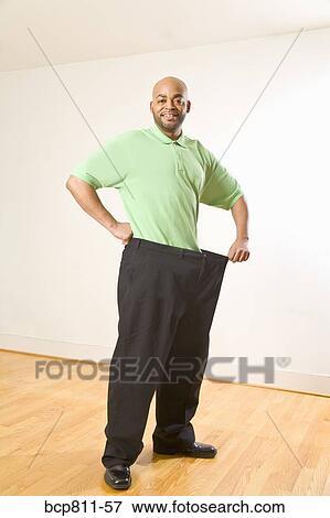 Stock Photo - African man holding out waistband of big pants. Fotosearch