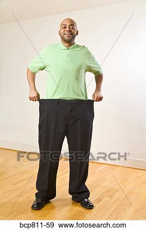 Stock Photo - African man holding out waistband of big pants. Fotosearch
