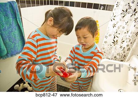 Stock Photo - Asian girl helping brother with tooth paste. Fotosearch