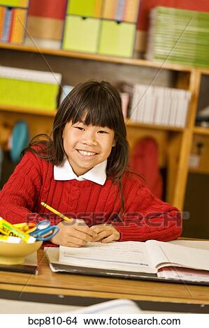 Picture - Asian girl writing at school desk. Fotosearch