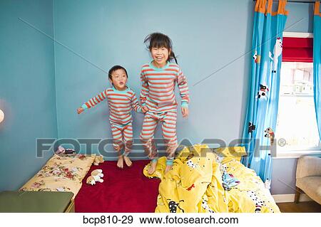 Stock Photo - Asian siblings jumping on bed. Fotosearch