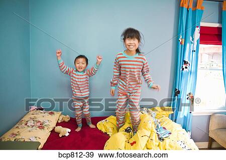 Stock Photo - Asian siblings jumping on bed. Fotosearch