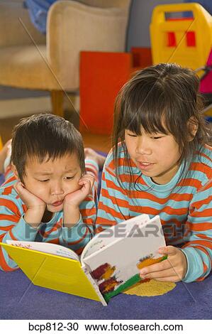 Stock Image - Asian siblings reading book. Fotosearch