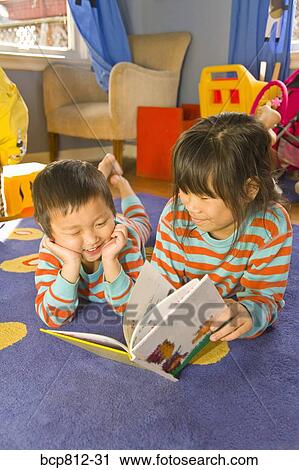 Stock Image - Asian siblings reading book. Fotosearch