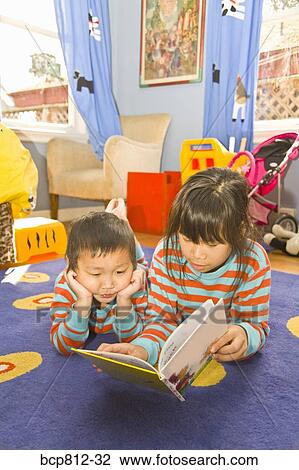 Stock Image - Asian siblings reading book. Fotosearch