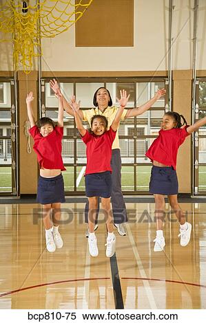 Stock Photography - Multi-ethnic girls and teacher jumping in school gym. Fotosearch