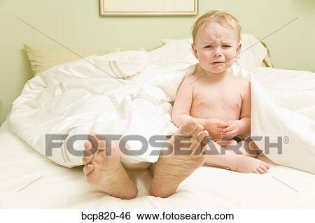 Stock Photograph - Baby crying as mother sleeps in bed. Fotosearch