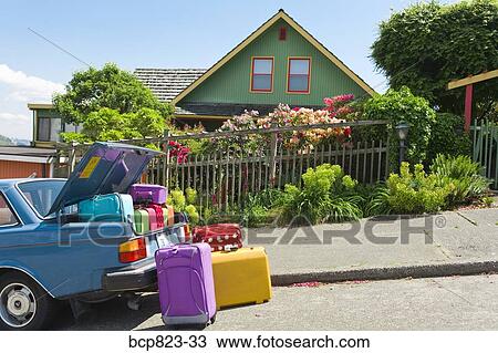 Stock Image - Car trunk loaded with colorful suitcases in front of house. Fotosearch