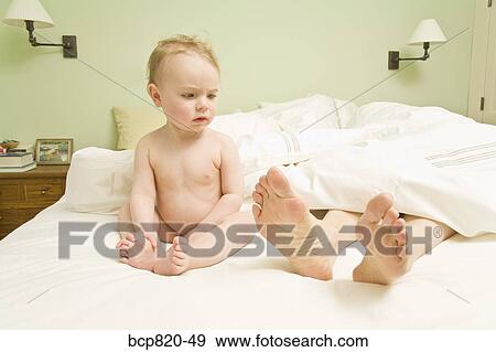 Stock Photo - Curious baby looking at mother’s feet in bed. Fotosearch