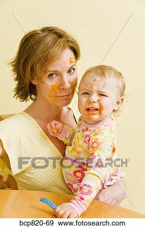 Stock Photo - Frustrated mother feeding messy baby. Fotosearch