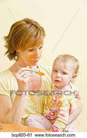 Frustrated mother trying to feed messy baby View Large Photo Image Stock Image - Frustrated mother trying to feed messy baby. Fotosearch