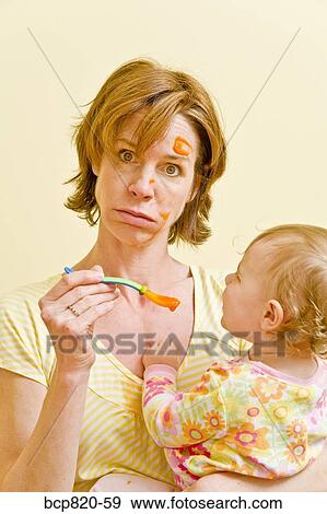 Frustrated mother trying to feed messy baby View Large Photo Image Stock Photo - Frustrated mother trying to feed messy baby. Fotosearch