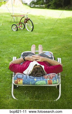 Man with magazine over face relaxing in lounge chair in backyard View Large Photo Image Stock Image - Man with magazine over face relaxing in lounge chair in backyard. Fotosearch