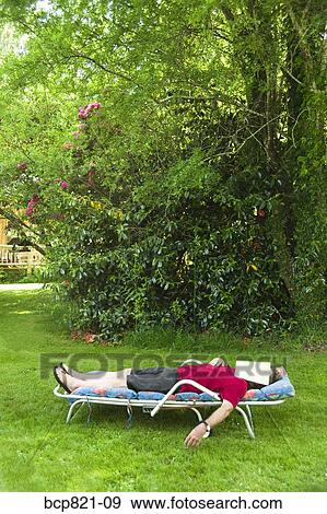 Stock Photo - Man with magazine over face relaxing in lounge chair in backyard. Fotosearch