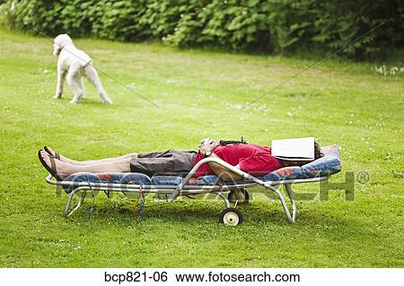 Stock Photograph - Man with magazine over face relaxing in lounge chair in backyard. Fotosearch