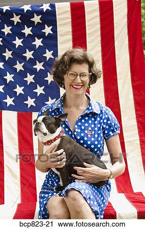 Stock Image - Patriotic woman and Boston Terrier dog posing with American flag. Fotosearch