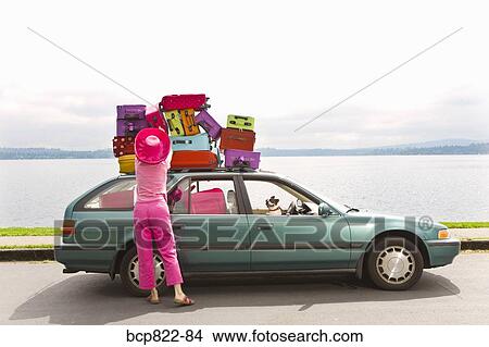 Woman adjusting stack of colorful suitcases on top of car View Large Photo Image Picture - Woman adjusting stack of colorful suitcases on top of car. Fotosearch