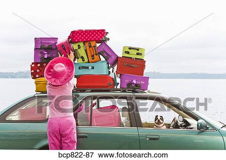 Stock Photo - Woman adjusting stack of colorful suitcases on top of car. Fotosearch