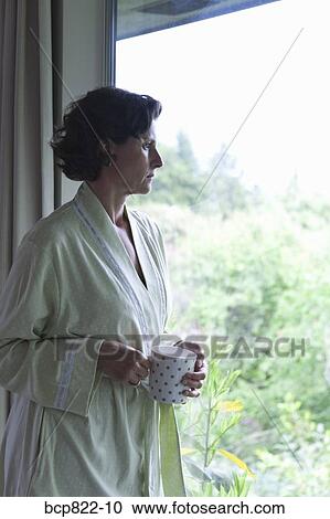 Stock Image - Woman drinking coffee and looking out window in the morning. Fotosearch