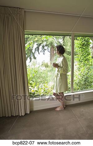 Stock Photo - Woman drinking coffee and looking out window in the morning. Fotosearch