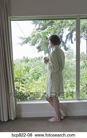 Stock Photo - Woman drinking coffee and looking out window in the morning. Fotosearch
