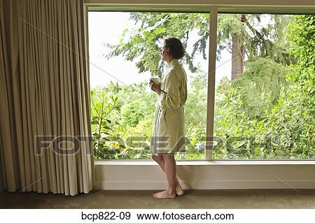 Stock Photo - Woman drinking coffee and looking out window in the morning. Fotosearch