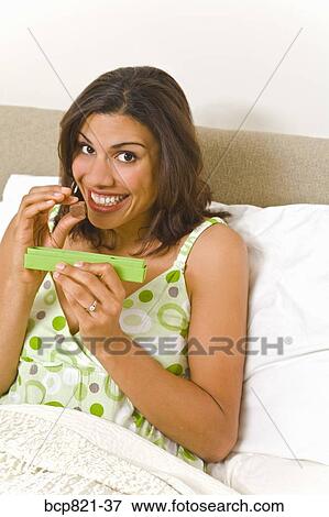Stock Photo - Woman eating chocolates in bed. Fotosearch